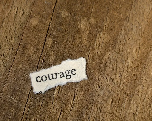 Een klein, rafelig afgescheurd stukje papier met de getypte tekst 'courage' ligt op een ruwe, houten plank